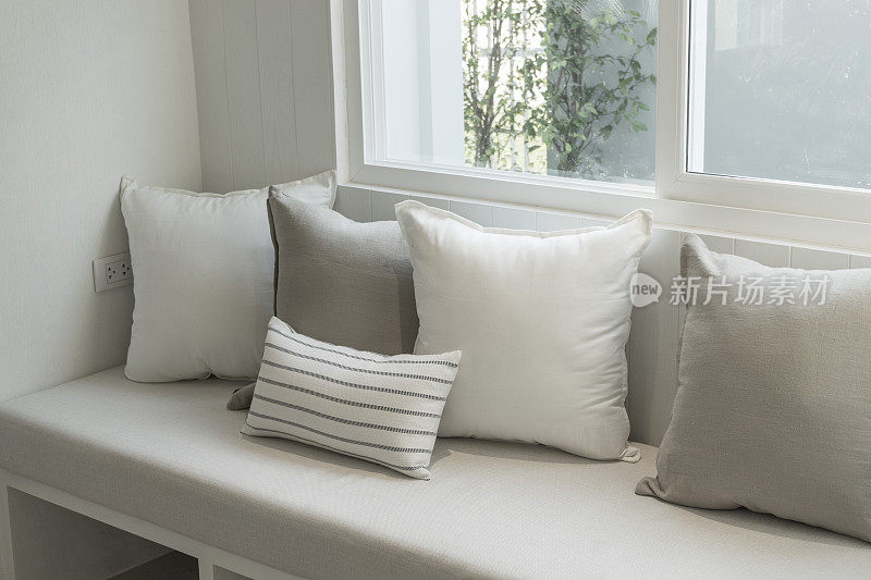 窗边有白色和灰色靠垫的舒适沙发。