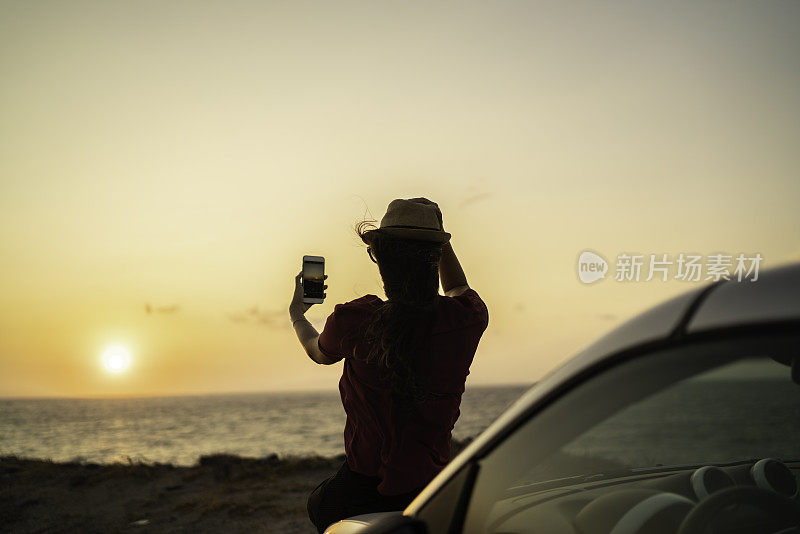 后视图的一个女人站在一辆汽车前，并采取了一个美丽的地方的照片