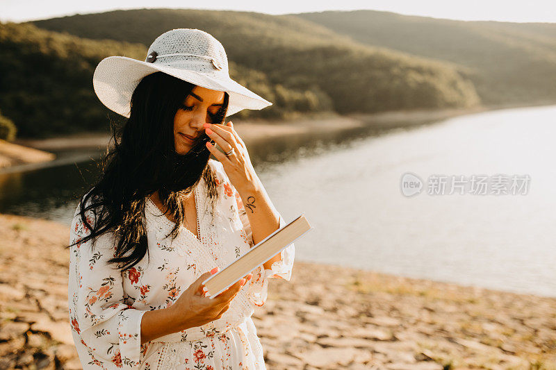年轻优雅的感性女性拿着一本书在湖边散步