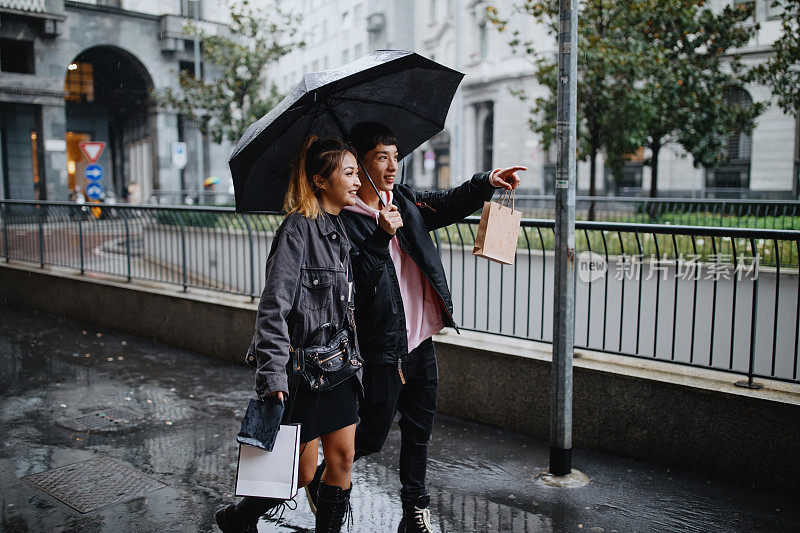 年轻夫妇撑着伞走在雨中的城市街道上