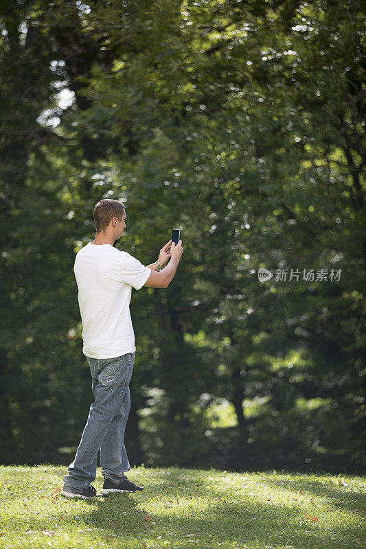 年轻成年男子在公园用手机拍照
