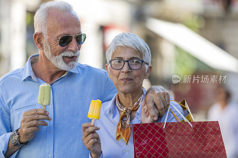 成熟的夫妇走在城市的大街上，在成功购物后吃冰淇淋