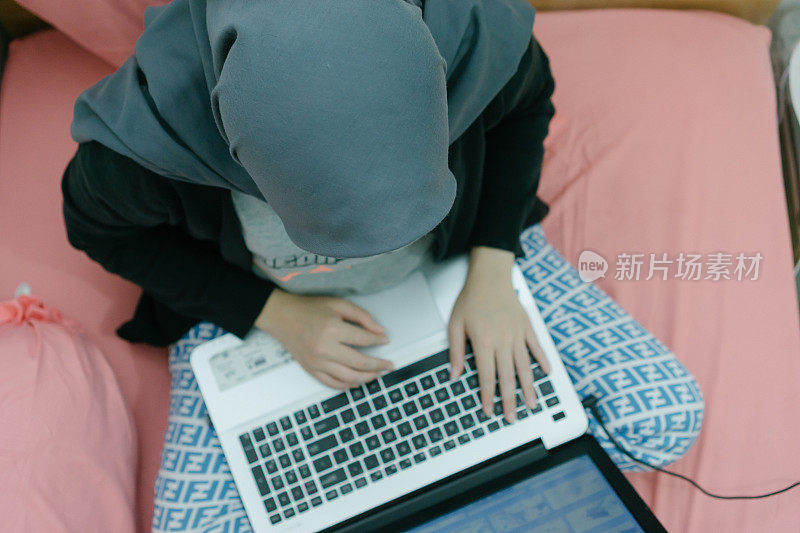 亚洲千禧一代年轻人戴着头巾在家卧床工作