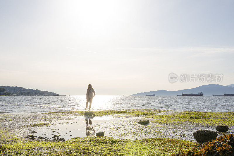 成熟的女人在日出时走过潮滩