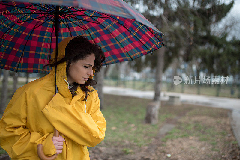 穿着黄色雨衣的年轻女子在公园里度过雨天