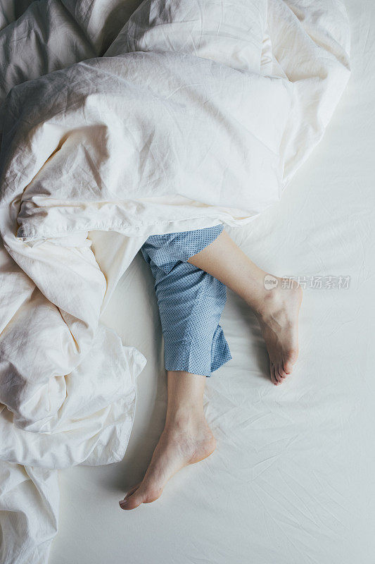 头顶裁剪的脚的一个白人妇女在蓝色睡衣躺在床上覆盖着羽绒被
