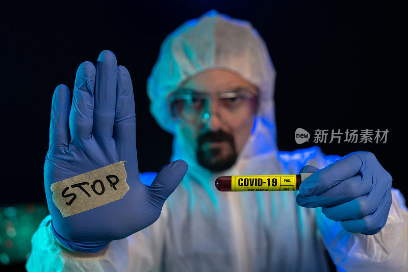 实验室科学家在实验室拿着冠状病毒血样，看着摄像机并显示停止标志