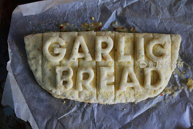 生蒜蓉面包的图片，贴着从生面团上剪下的字母，上面写着“蒜蓉面包”