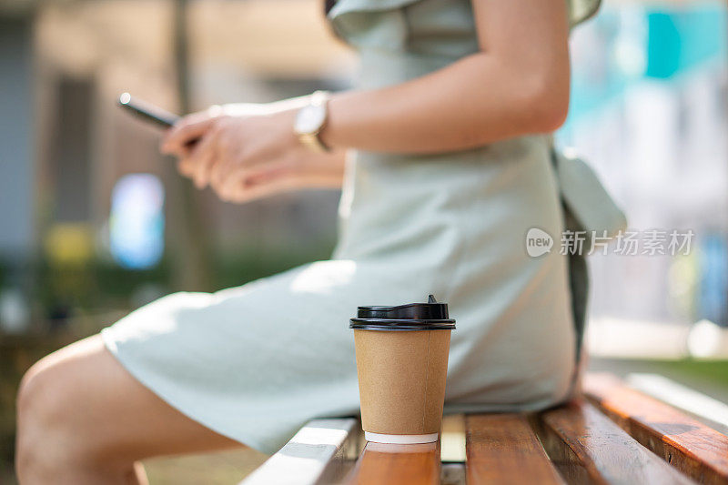 年轻的亚洲女子使用智能手机，旁边放着一杯外卖咖啡