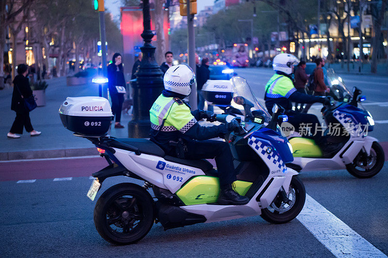 傍晚，交警骑着摩托车在十字路口巡逻。城市背景的巡逻警察。巡逻和守卫警察。西班牙巴塞罗那警方的交通工具