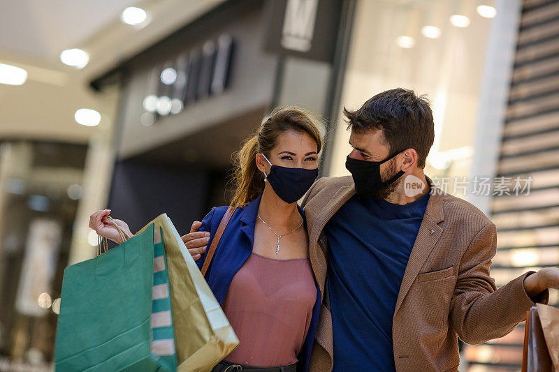 这对年轻夫妇提着购物袋，在商场里走来走去，两人都戴着防护口罩，面面相觑，疫情期间的生活
