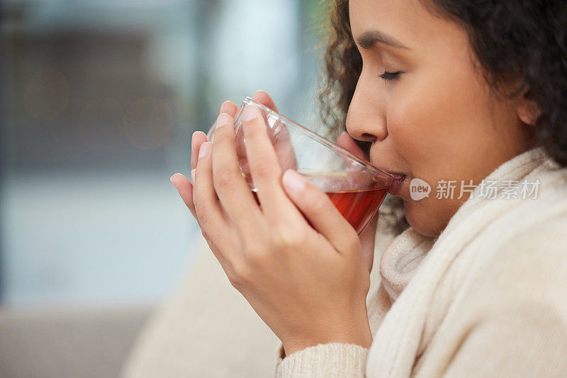 一个漂亮的年轻女子坐在家里的沙发上喝着一杯花草茶