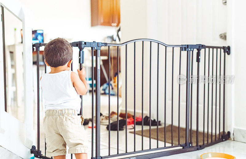 一个蹒跚学步的男孩被困在客厅的婴儿门在家里的安全