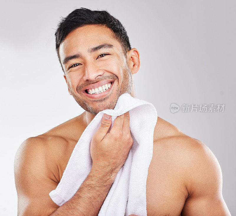 一名英俊的年轻男子的画室肖像，在灰色背景下摆姿势，用毛巾擦干自己