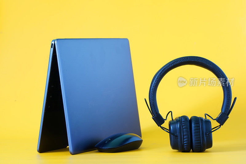 这款笔记本配有耳机和黄色背景的电脑鼠标。使用现代无线技术和互联网收听音频博客、音乐和播客的概念