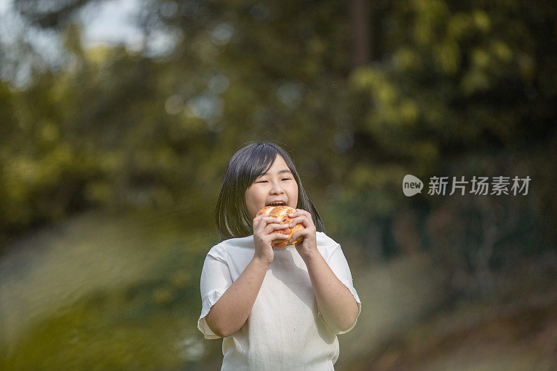 亚洲中国可爱的小女孩喜欢在阳光明媚的日子里在公园里吃她最喜欢的面包
