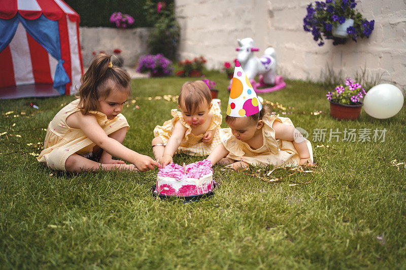 一对双胞胎姐妹和一个姐姐在草地上玩在他们的第一个生日派对