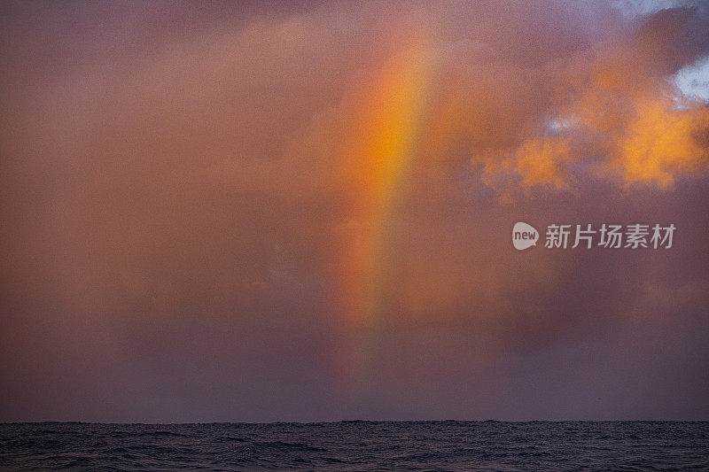 明亮生动的彩虹在暴风雨的背景下，在开阔的海洋表面水平