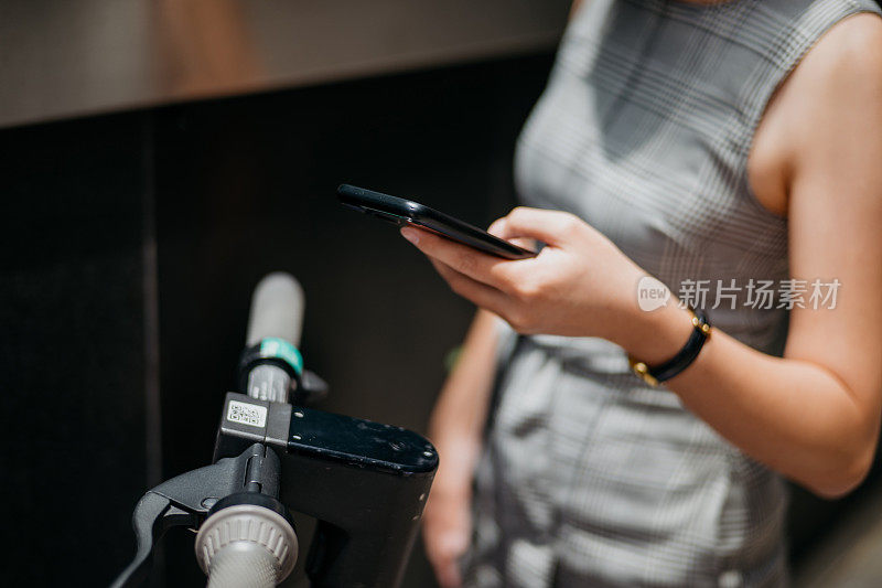 亚洲女商人用智能手机扫描二维码激活电动滑板车