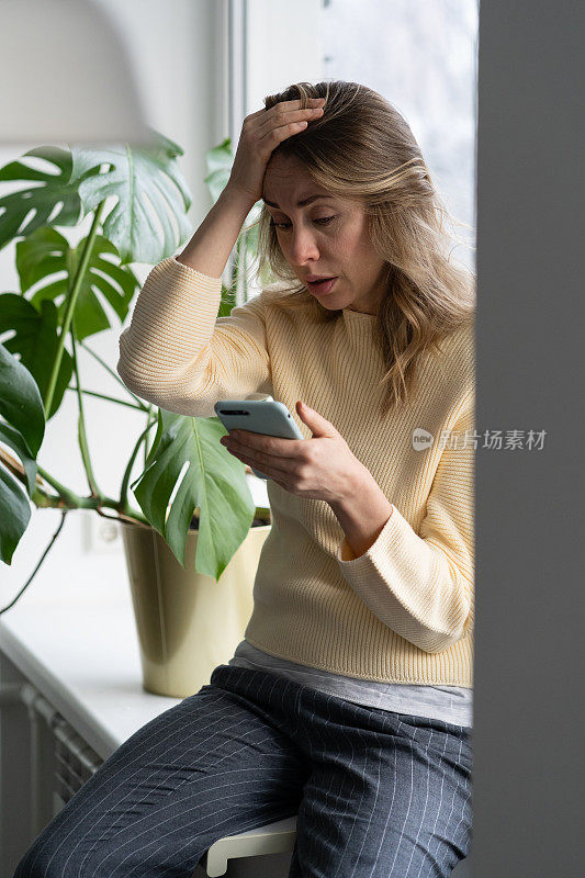 抑郁的中年妇女拿着智能手机在家里读不愉快的短信接收坏消息。