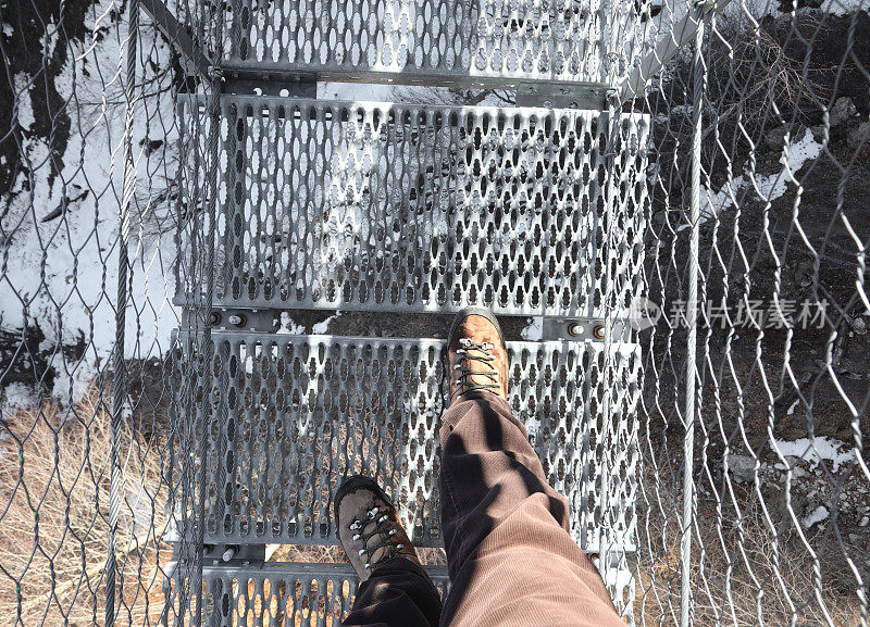 徒步旅行者穿过虚空中的吊桥时穿的登山靴