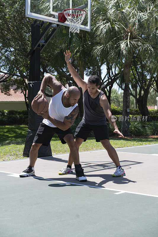 一名篮球运动员在室外球场处理球和旋转，而另一名球员在阻挡