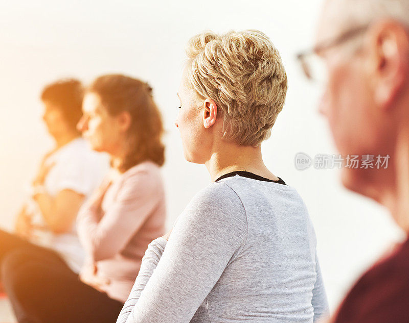 成熟的男人和女人在禅瑜伽课上莲花姿势冥想。一群瑜伽修行者坐在一起，寻找内心的平衡与安宁。练习镇静呼吸练习和意识