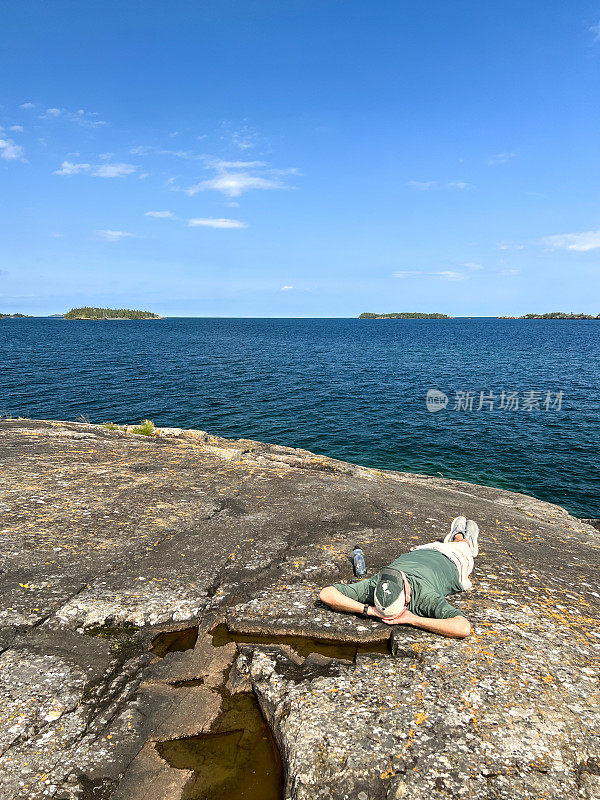 一个单身男子躺在苏必利尔湖的岩石海岸