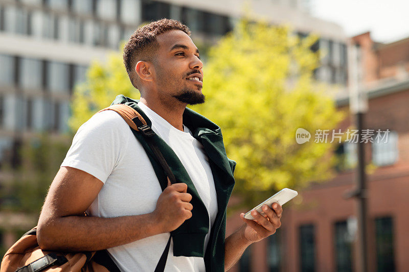 英俊的非裔美国大学生在户外使用智能手机，下课后在市区散步