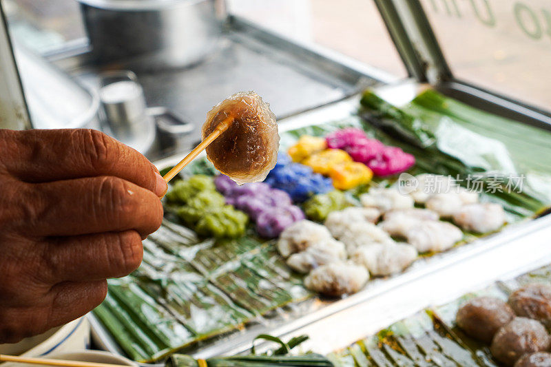 这是一张特写照片，展示的是一只手拿着一个漂亮的、圆形的、透明的泰国蒸猪肉饺子准备吃。