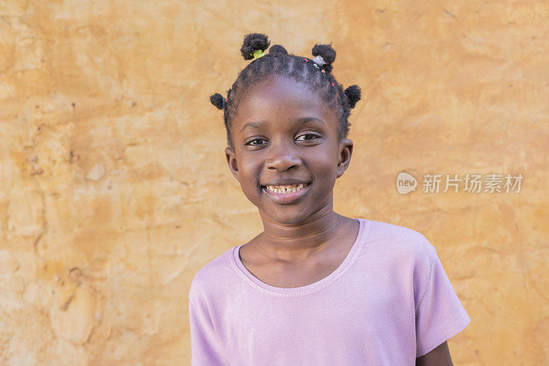 一个快乐的美国黑人小女孩的肖像在户外墙的背景前微笑