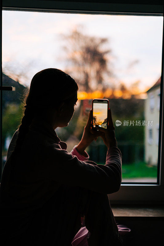 年轻的白人妇女在家里的窗户上拍摄日落。