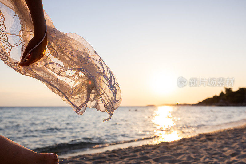 日落时分，一个不知名的女人穿着背心裙走在沙滩上