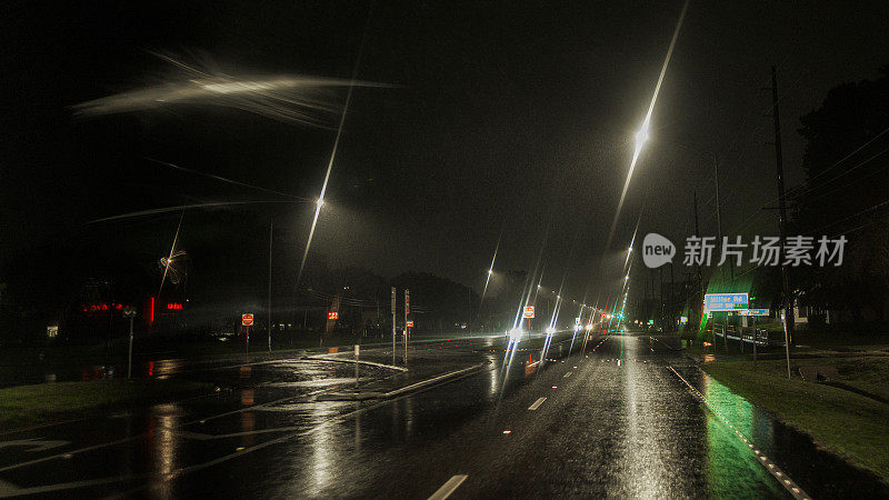 暴雨后夜间驾驶:在暴雨中在潮湿的道路上行驶。被照亮的街道和远处散焦的光迹。柔焦，镜头光晕。驱动板