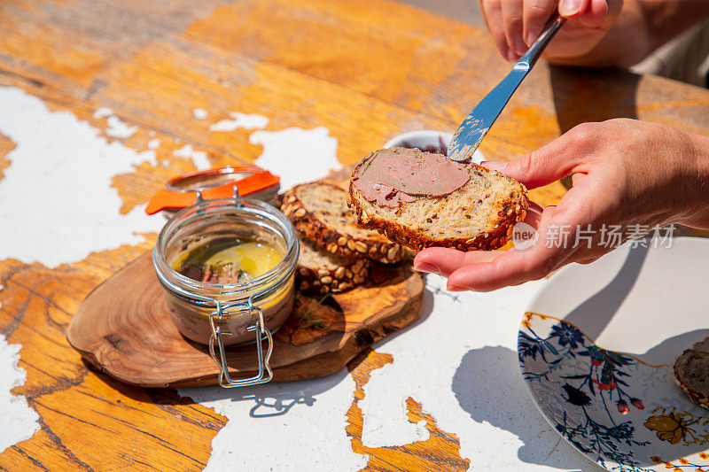 用餐刀将鹅肝酱涂在餐桌上的一片全麦面包上