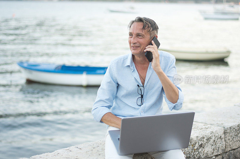 自由职业者在海滩上用手机和笔记本电脑咨询