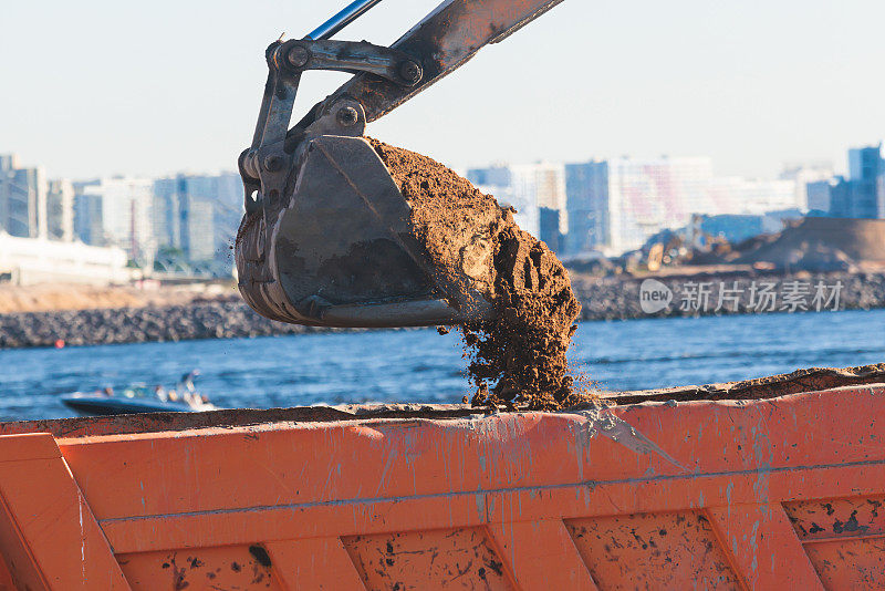 挖掘机在施工现场将沙子卸入自卸车，在道路施工期间进行挖掘和工作，反铲和自卸车卸载道路金属和砾石，施工新路