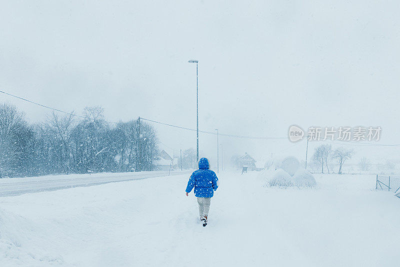 一名穿着蓝色外套的女子在大雪中漫步在斯堪的纳维亚村庄的街道上，欣赏冬天