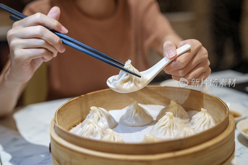 用筷子夹着小笼包的女性手特写，这是一种放在竹制蒸笼里的中国传统食物。