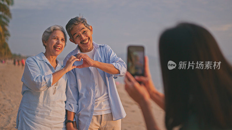 老夫妇一家在海滩上与当地导游一起享受，而她用智能手机拍照。