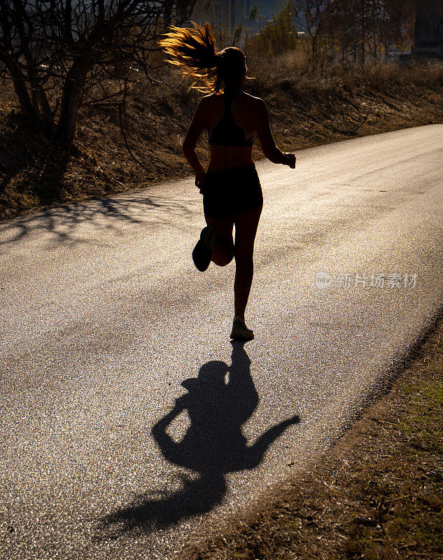 一个身材匀称的年轻女运动员，在黎明的背光下，以完美的风格在一条铺好的山路上奔跑，她的头发在空中飘散，倒投在铺好的路上。