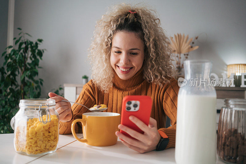 卷发的女人一边吃早餐一边用手机