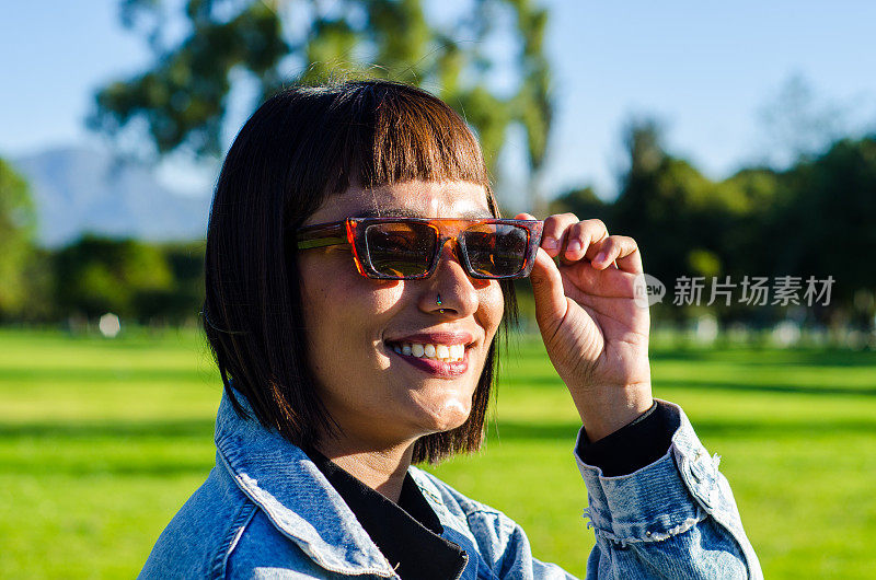 在一个阳光明媚的日子里，一名剪短头发的年轻女子在公园里穿着休闲服，戴着太阳镜