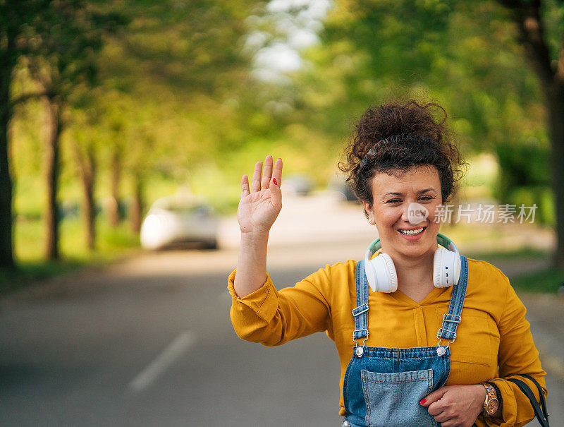 一个微笑的女人站在街上向某人挥手。