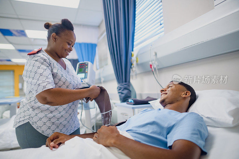 在繁忙的医院病房里，友善的女护士在病床上检查戴助听器的年轻男性的生命体征