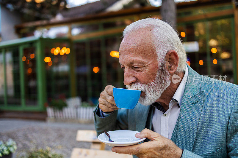 有思想的成熟男人在咖啡馆里喝咖啡，然后看向别处。一幅大胡子老人在咖啡馆喝咖啡的画像。