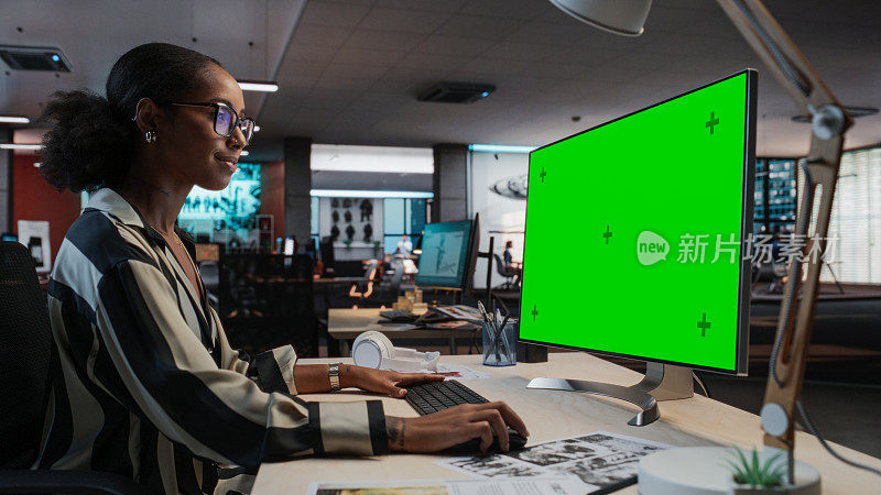 富有创造力的黑人女性的肖像坐在桌子上使用桌面电脑与模拟绿屏。女性概念美工在游戏设计初创公司工作，创造沉浸式游戏玩法