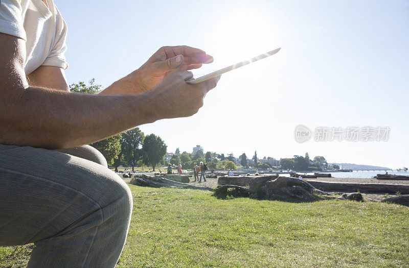 一名男子在海滩附近的长椅上休息，用着数码平板电脑