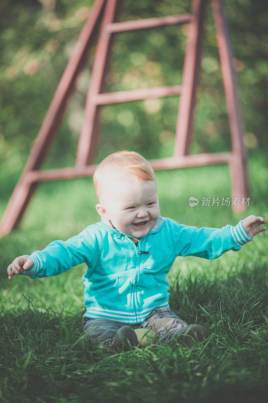 可爱的红发小男孩在苹果园的草地上玩耍