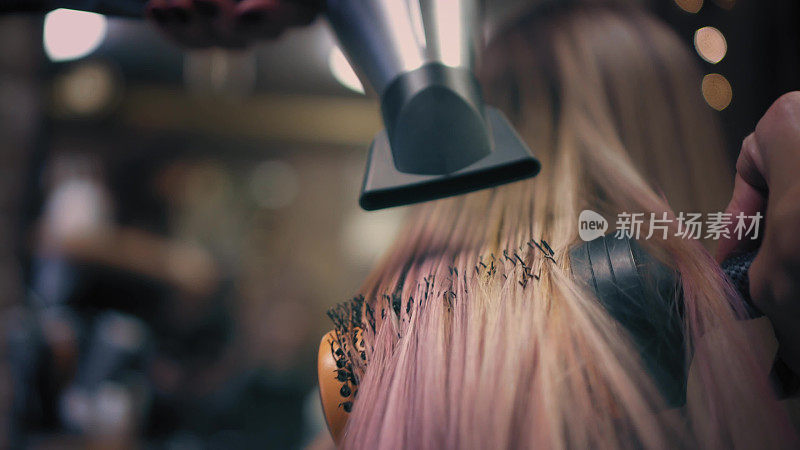 美发师用吹风机和专业的圆发刷将女人的长金发拉直。底视图